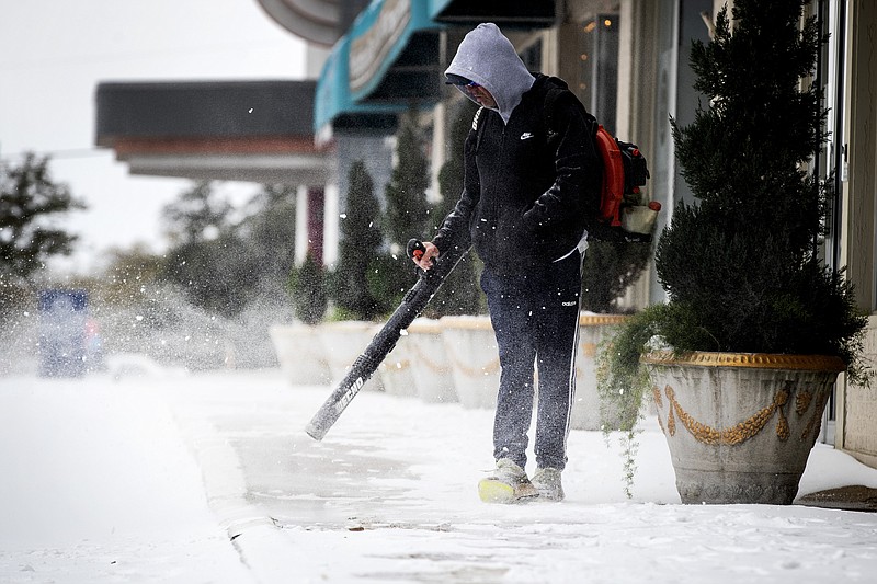 Scott Blocker uses a blower to clear the sidewalks of snow  in front of a shopping center on Camp Bowie Blvd. Wednesday, Feb. 17, 2021, in Fort Worth, Texas. (Yffy Yossifor/Star-Telegram via AP)