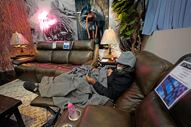 Natalie Harrell holds her sleeping daughter, Natasha Tripeaux while sitting in a recliner at a Gallery Furniture store after the owner opened his business as a shelter for those without power at homes Tuesday, Feb. 16, 2021, in Houston. More than 4 million people in Texas still had no power a full day after historic snowfall and single-digit temperatures created a surge of demand for electricity to warm up homes unaccustomed to such extreme lows, buckling the state's power grid and causing widespread blackouts. (AP Photo/David J. Phillip)