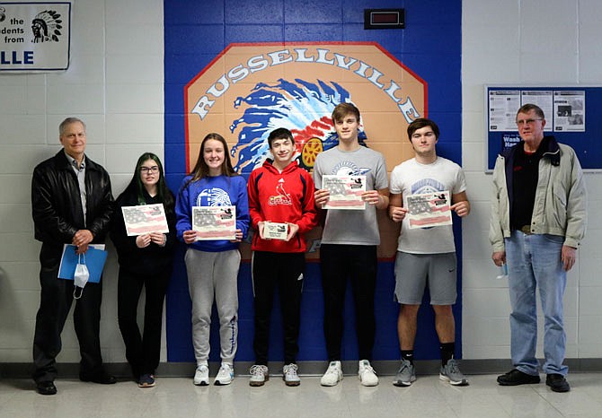 From left, Chris Jarboe; Russellville sophomores Emily Jurgle, Cameron Grayson, Kameron Hogue, Charlie Miller and Josiah Herman; and Don Hentges stand in front of the Russellville High School logo on Friday as the students are recognized by Operation Bugle Boy for their letters of appreciation to veterans. 