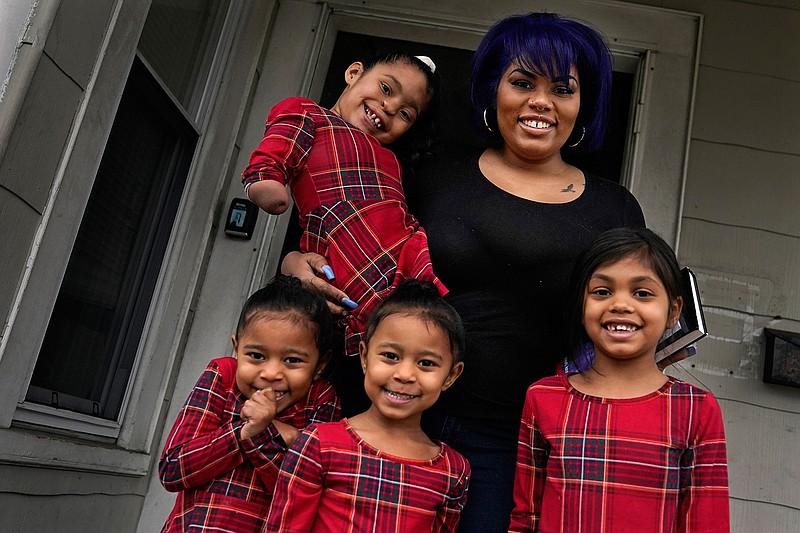 Dinora Torres, a MassBay Community College student, poses with her four daughters on the front porch of their home, Thursday, Jan. 14, 2021, in Milford, Mass. From front left are daughters Davina, Alana and Hope, with Faith in Dinora's arms. At the college, applications for meal assistance scholarships have increased 80% since last year. Among the recipients is Torres, who said the program helped keep her enrolled. (AP Photo/Charles Krupa)