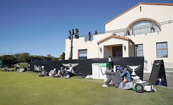 Players and caddies lounge on the practice green after high winds suspended play during Saturday's third round of the Genesis Invitational at Riviera Country Club in the Pacific Palisades area of Los Angeles.