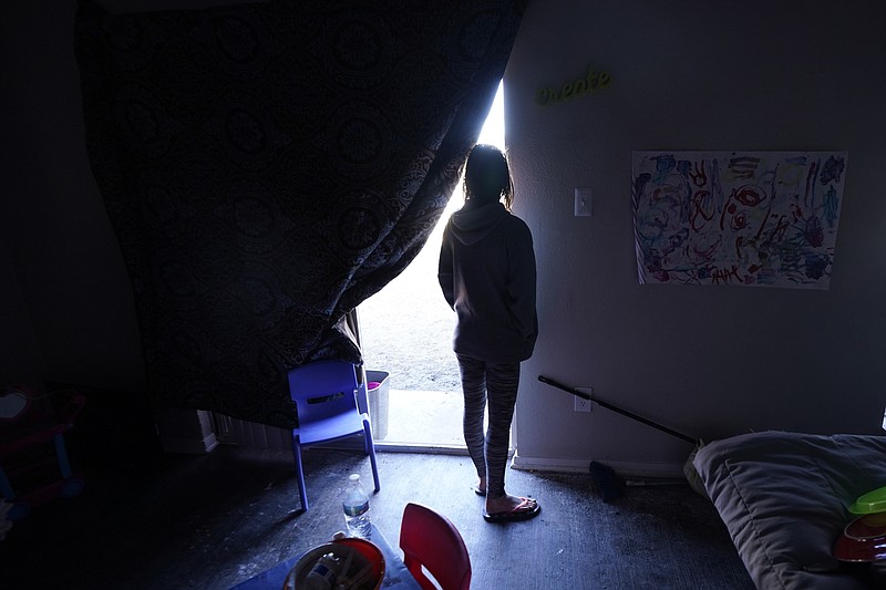 FILE - In this Feb. 23, 2021, file photo, Ricki Mills looks out from her home as she waits for a fire hydrant to be turned to get water,  in Dallas. The single mother had her apartment flooded last week by a pipe that burst during the record winter cold and was waiting for repairs to restore water to the apartment complex. On Thursday, Feb. 25, 2021 managers of Texas' power grid are expected to receive a lashing in the first public hearings about the crisis at the state Capitol. (AP Photo/LM Otero File)