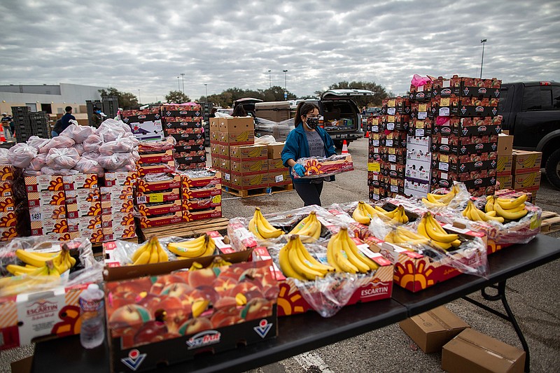 In this Feb. 21, 2021 file photo, a volunteer carries food to be distributed during the Neighborhood Super Site food distribution event organized by the Houston Food Bank and HISD, in Houston. The recent winter storm nightmare knocked out power to more than 4 million customers across the state. On Thursday, Feb. 25 managers of Texas' power grid are expected to receive a verbal lashing in the first public hearings about the crisis at the state Capitol. (Marie D. De Jess/Houston Chronicle via AP, File)