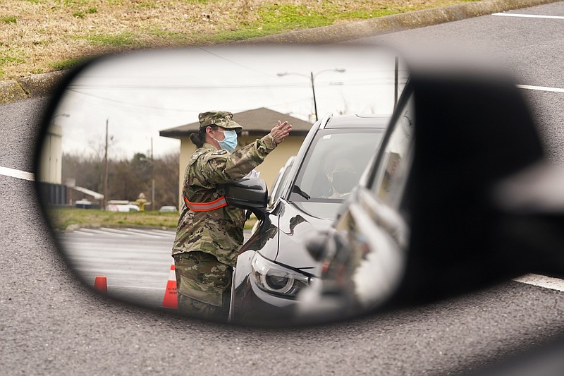 A National Guard soldier directing drivers is reflected in the mirror of a car waiting in a COVID-19 vaccination line Feb. 26, 2021, in Shelbyville, Tenn. Tennessee has continued to divvy up vaccine doses based primarily on how many people live in each county, and not on how many residents belong to eligible groups within those counties. (AP Photo/Mark Humphrey)