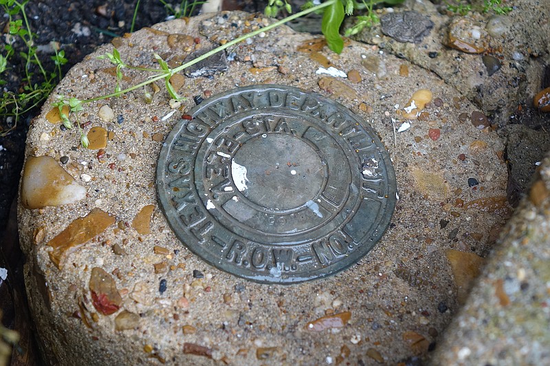 This official-looking circular cement marker is almost hidden along the sidewalk of William Street near East Hiram in downtown Atlanta, Texas. It is a benchmark survey monument indicating Farm to Market 251 passes here.
