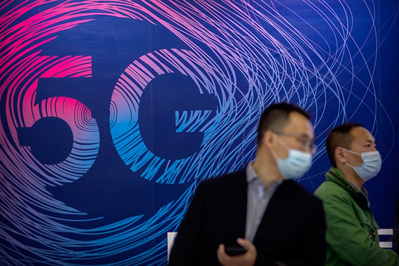 People wearing face masks to protect against the spread of the coronavirus walk past a display advertising 5G wireless services at the PT Expo in Beijing, Wednesday, Oct. 14, 2020. Chinese leaders are shifting focus from the coronavirus back to long-term goals of making China a technology leader at this year's highest-profile political event, the meeting of its ceremonial legislature, amid tension with Washington and Europe over trade, Hong Kong and human rights. (AP Photo/Mark Schiefelbein)