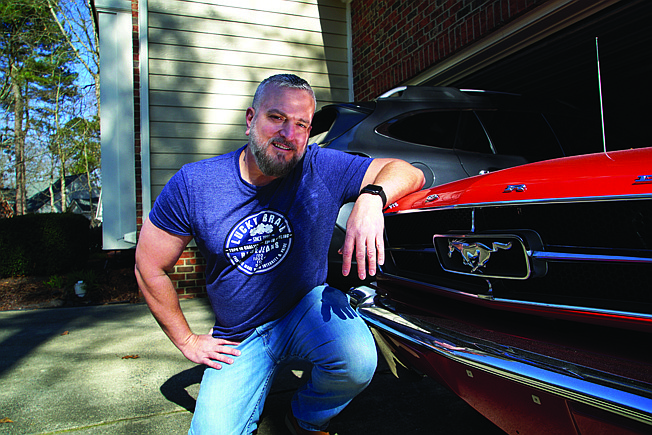 Steve Bock kneels beside his 1965 Ford Mustang at his home March 5 in Apex, N.C. He recently bought a Subaru Outback, but would like to have an electric or hybrid car if the prices ever come down enough. 