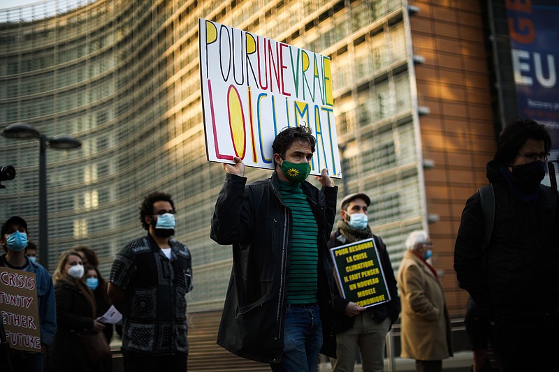 A man holds a placard that reads in French: "For a real climate law" as he listens speeches with others during a small climate protest outside EU headquarters in Brussels, Thursday, March 25, 2021. The European Union's top court has rejected an effort by a Scandinavian youth group and eight families around the world to force the EU to set more ambitious targets for reducing greenhouse gas emissions. (AP Photo/Francisco Seco)