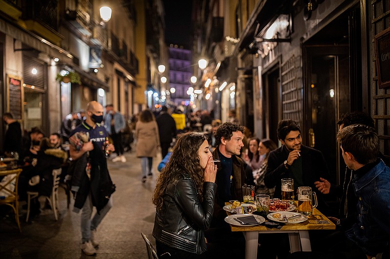 Tourists and locals have drinks at a bar in downtown Madrid, Spain, Friday, March 26, 2021. With its policy of open bars and restaurants — indoors and outdoors — and by keeping museums and theaters running even when outbreaks have strained hospitals, Madrid has built a reputation as an oasis of fun in Europe's desert of restrictions. Other Spanish regions have a stricter approach to entertainment. Even sunny coastal resorts offer a limited range of options for the few visitors that started to arrive, coinciding with Easter week, amid a set of contradictory European travel rules. (AP Photo/Bernat Armangue)