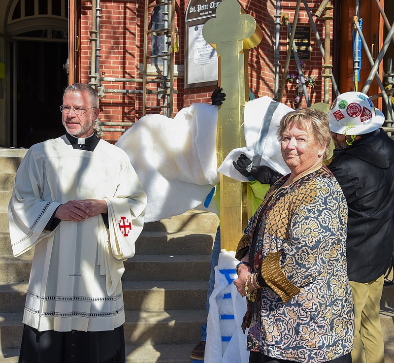 Julie Smith/News Tribune
Edie Vogel, right, poses with Fr. Jeremy Secrist as the pair stand in front of the new cross following a blessing ceremony at St. Peter Church Monday. The cross was then placed atop the steeple which rises approximately 130 feet in the air. Vogel donated funds to have the cross gilded in order to preserve the shine are prevent the oxidation and dulling of the finish. The original copper cross was taken down Nov. 19, 2020 and sent to Renassaince Roofing in Belvidere, Illinois where the old one was used as a template to construct a new shroud and cross. Vogel made the donation in the name of her great-great grandparents GH and Anna Marie Dulle, who donated the bricks used in construction of the church and rectory in 1883. Edie said that today (Monday) would have been her mother, Rose Mary's, 104th birthday. Vogel credits her mother's wise spending and savings habits for the money to allow this donation.