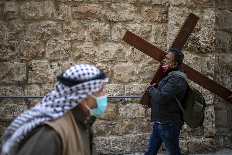 A Christian carries a cross as he walks along the Via Dolorosa towards the Church of the Holy Sepulchre, traditionally believed by many to be the site of the crucifixion of Jesus Christ, during the Good Friday procession in Jerusalem's old city, Friday, April 2, 2021. (AP Photo/Ariel Schalit)