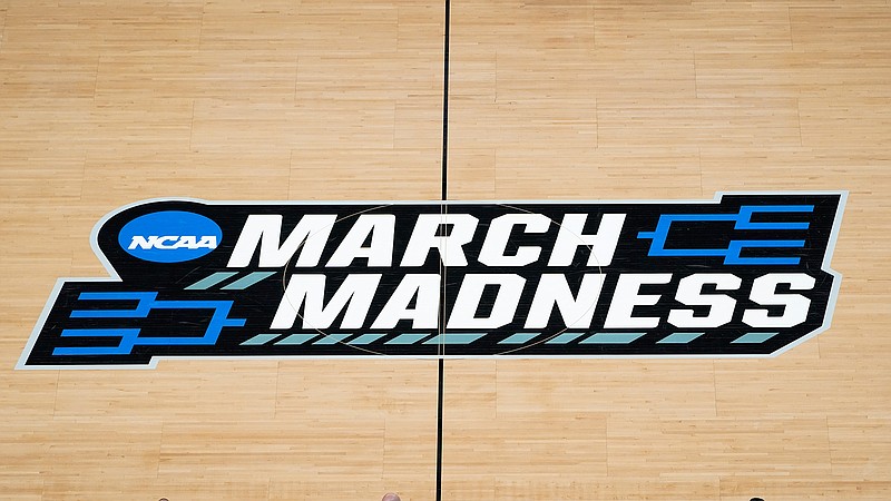 In this March 20, 2021, file photo the March Madness logo is shown on the court during the first half of a men's college basketball game in the first round of the NCAA tournament at Bankers Life Fieldhouse in Indianapolis. A Supreme Court case being argued this week amid March Madness could erode the difference between elite college athletes and professional sports stars. (AP Photo/Paul Sancya, File)