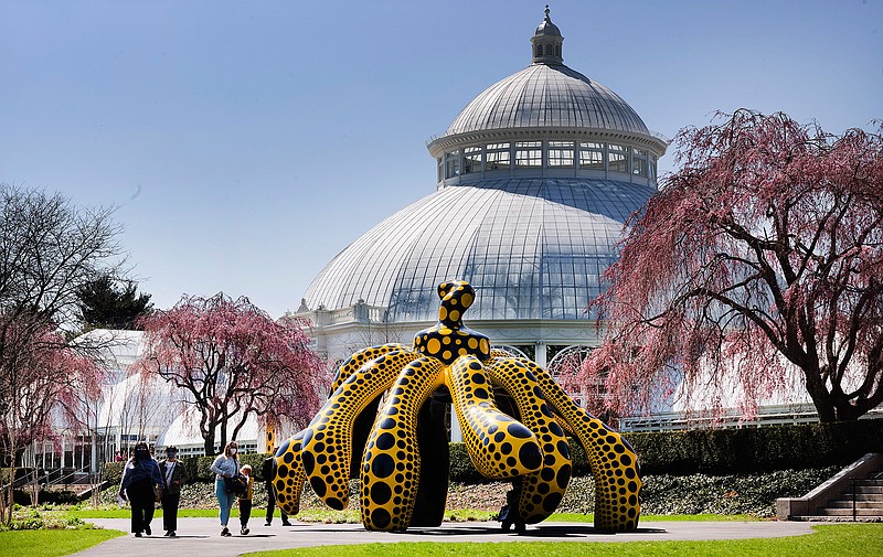 People walk by one of Yayoi Kusama's pumpkin sculptures at the New York Botanical Garden, Thursday, April 8, 2021 in New York. The expansive exhibit has opened, and ticket sales have been brisk in a pandemic-weary city hungry for more outdoor cultural events. (AP Photo/Mark Lennihan)