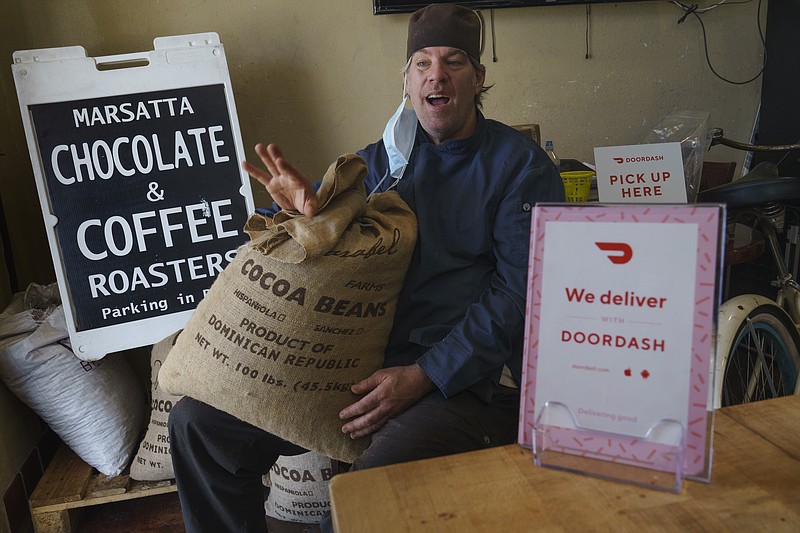 Jeffray Gardner, the owner of Marsatta Chocolate poses with a bag of cocoa beans at his company's office in Torrance, Calif., Sunday, March 28, 2021.  Restaurants and delivery companies remain uneasy partners, haggling over fees and struggling to make the service profitable for themselves and each other.  Gardner says he probably loses money on the one or two delivery orders he gets each day.  But he’s still happy to work with delivery companies because they help him reach a wider audience.  (AP Photo/Damian Dovarganes)