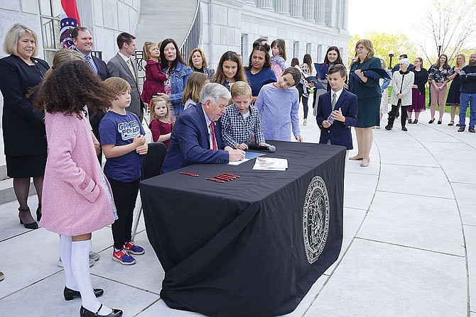 Gov. Mike Parson signs two bills outside the Missouri Capitol steps on Thursday that will increase tax credits available to adoptive and foster families and those who donate to domestic violence centers and rape crisis centers. Lawmakers involved with the legislation and children were able to add their signatures to the bill in a ceremony alongside Parson and first lady Teresa Parson.