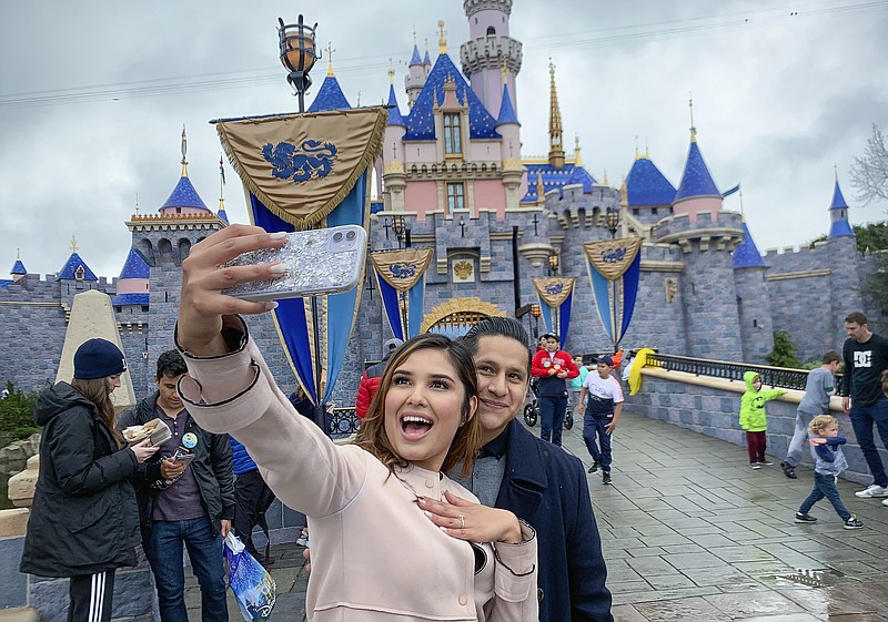 FILE - In this March 13, 2020, file photo, Katherine Quezada shows off her engagement ring as she takes a selfie with her new fiance, Fernando Carranza, in front of Sleeping Beauty Castle the during the last day before Disneyland closes because of the COVID-19 coronavirus outbreak, in Anaheim, Calif. Carranza proposed to Quezada in front of the castle earlier that day. Disneyland Park and Disney California Adventure park will reopen to visitors on Friday, April 30, 2021. (Jeff Gritchen/The Orange County Register via AP, File)