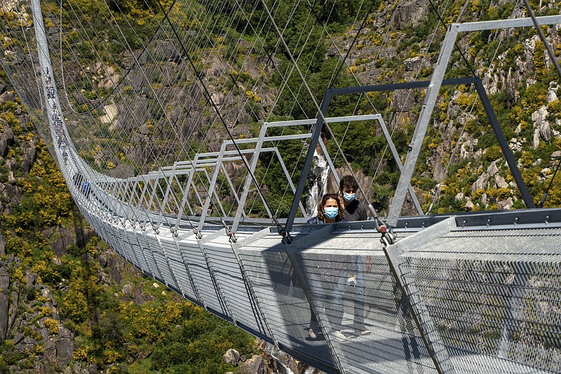 People walk across a narrow footbridge suspended across a river canyon, which claims to be the world's longest pedestrian bridge, in Arouca, northern Portugal, Sunday, May 2, 2021. The Arouca Bridge inaugurated Sunday, offers a half-kilometer (almost 1,700-foot) walk across its span, some 175 meters (574 feet) above the River Paiva. (AP Photo/Sergio Azenha)