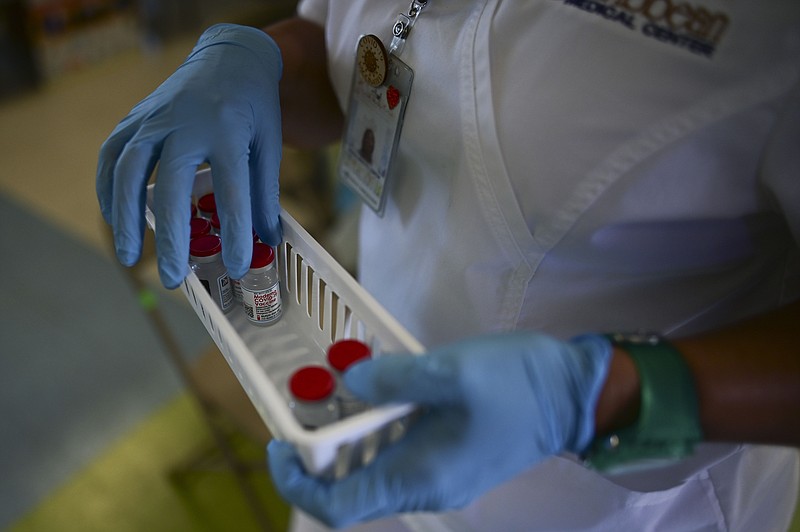 FILE - In this March 10, 2021 file photo, a nurse carries vials of the Moderna COVID-19 vaccine during a mass vaccination campaign, at the Maria Simmons elementary school in Vieques, Puerto Rico. A spike in cases and hospitalizations has put medical experts at odds with the government, which is struggling to protect people’s health while also trying to prevent an economic implosion on an island battered by hurricanes, earthquakes and a prolonged financial crisis. (AP Photo/Carlos Giusti, File)