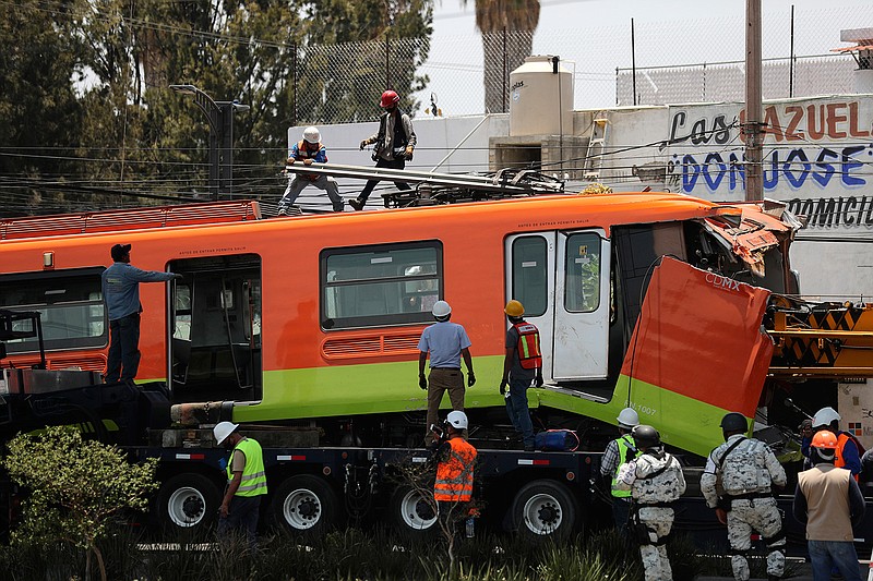 Workers remove a damaged subway car after it was lowered, with the help of a crane, to the ground from a collapsed elevated section of the metro, in Mexico City, Tuesday, May 4, 2021. The elevated section of the metro collapsed late Monday, killing at least 24 people and injuring at least 79, city officials said. (AP Photo/Marco Ugarte)