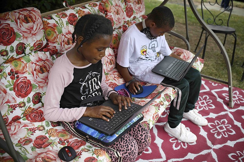 FILE - In this Friday June 5, 2020, file photo, fourth-grader Sammiayah Thompson, left, and her brother, third-grader Nehemiah Thompson, work outside in their yard on laptops provided by their school system for distant learning in Hartford, Conn. Americans can begin applying for $50 off their internet bill on Wednesday, May 12, 2021, as part of an emergency government program to keep people connected during the pandemic. (AP Photo/Jessica Hill, File)