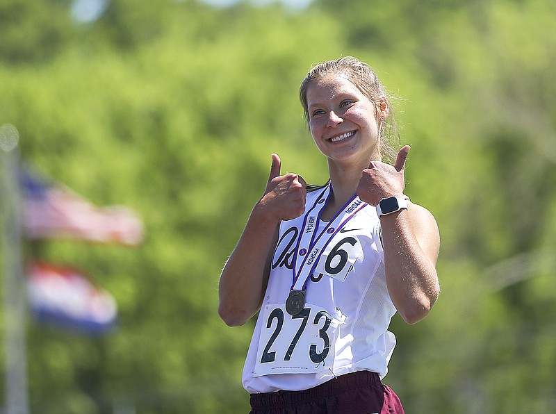 Sara Wolf from School of the Osage grins and flashes a double thumbs-up at the crowd after receiving the first-place medal for the 1,600-meter run Saturday at Adkins Stadium.