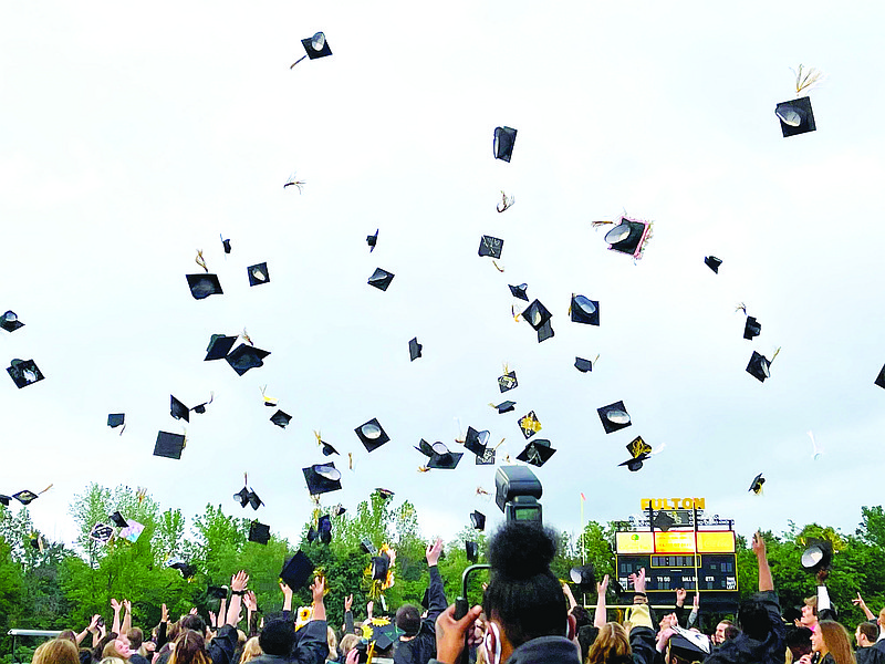 Members of the Fulton High School Class of 2021 huddle together one more time and throw their caps in the air to mark their graduation Friday evening.