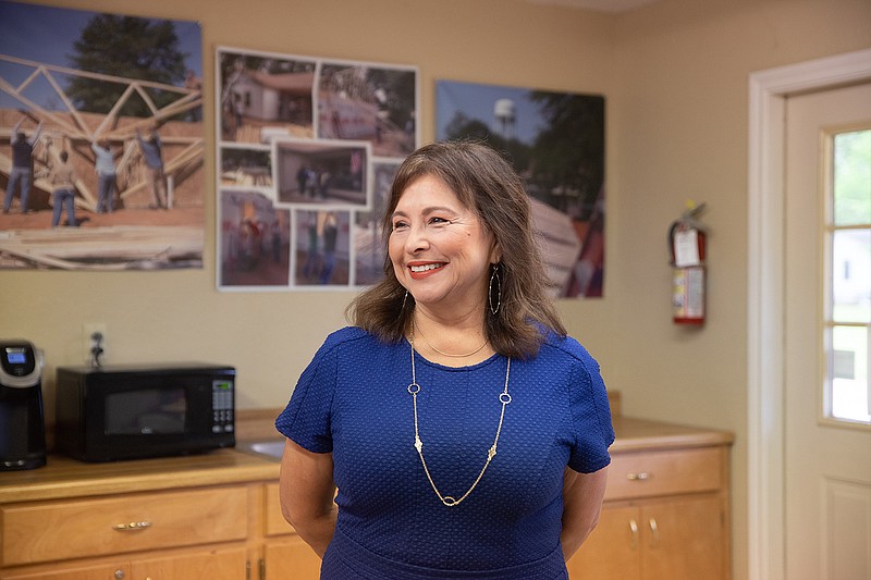 Mary Wormington, executive director for Habitat for Humanity of Texarkana, poses in front of photos of HFH's previous projects in their offices off of Robison Road in Texarkana.