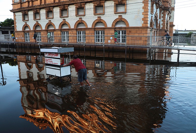 A street vendor pushes his mobile stall through a street flooded by the Negro River, in downtown Manaus, Amazonas state, Brazil, Tuesday, June 1, 2021. Rivers around Brazil's biggest city in the Amazon rain forest have swelled to levels unseen in over a century of record-keeping, according to data published Tuesday by Manaus' port authorities. (AP Photo/Edmar Barros)