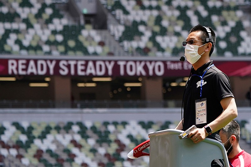 An official wears a face mask as he uses a starter pistol to signal the start a women's 100 meter heat at an athletics test event for the Tokyo 2020 Olympics Games at National Stadium in Tokyo, Sunday, May 9, 2021. Japan, seriously behind in coronavirus vaccination efforts, is scrambling to boost daily shots as the start of the Olympics in July closes in. (AP Photo/Shuji Kajiyama)