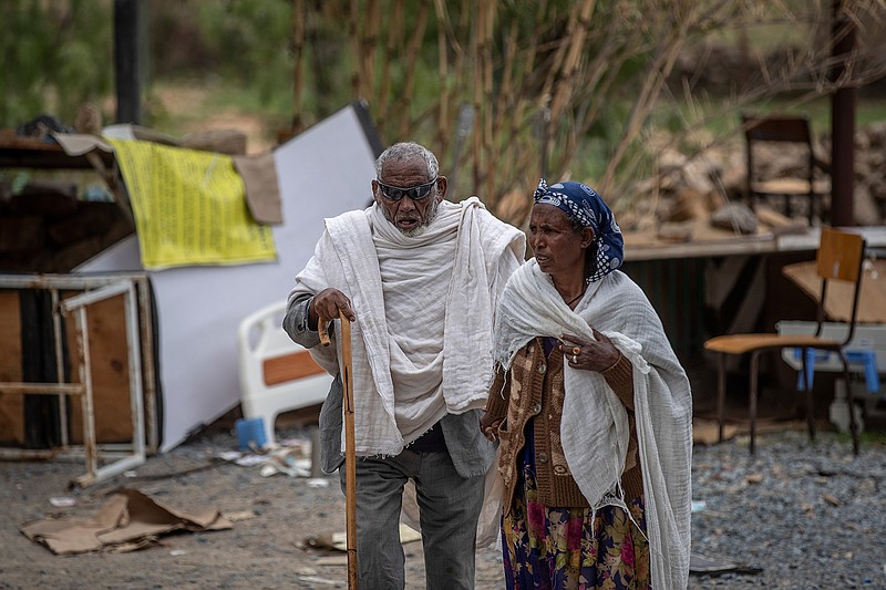 A woman leads a blind man to a visiting doctor, past destroyed furniture and other items in the driveway of a hospital which was damaged and looted by Eritrean soldiers who used it as a base, according to witnesses, in Hawzen, in the Tigray region of northern Ethiopia, on Friday, May 7, 2021. The battle for Hawzen is part of a larger war in Tigray between the Ethiopian government and the Tigrayan rebels that has led to the flight of more than 2 million of the region's 6 million people. (AP Photo/Ben Curtis)