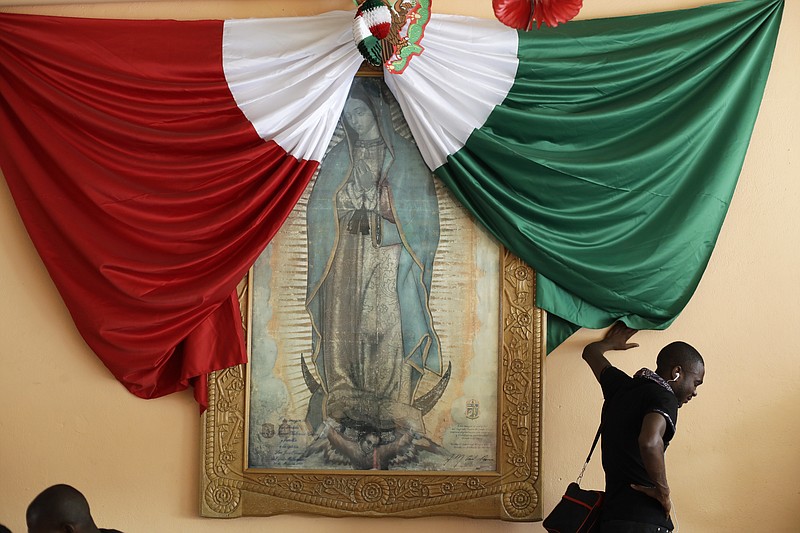 FILE - A Haitian man listening to music leans against a wall with the Mexican national flag and a framed image of the Virgin of Guadalupe, as he waits for a bed at the Padre Chava migrant shelter Monday, Sept. 26, 2016, in Tijuana, Mexico.Though Haitians living in the U.S. rejoiced when a recent extension was granted, Homeland Security Secretary Alejandro Mayorkas pointedly noted that it doesn't apply to Haitians outside the U.S. and said those who enter the country may be flown home. That means bleak choices for many Haitians who fled Haiti sometime after a 2010 earthquake, initially escaping to South America and later to Mexican cities that border the United States. (AP Photo/Gregory Bull)