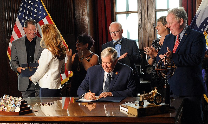 Governor Parson signs a bill into law Monday creating a statewide drug monitoring program. Coach Jim Marshall, left, receives the first signed copy of the bill in honor of his son, Cody.