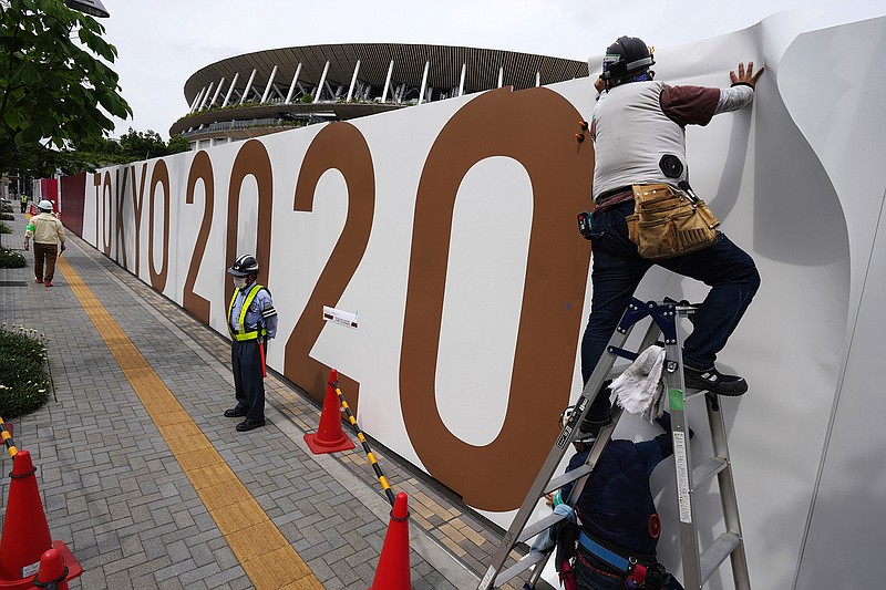 Workers paste the overlay on the wall of the National Stadium, where opening ceremony and many other events are scheduled for the postponed Tokyo 2020 Olympics, Wednesday, June 2, 2021, in Tokyo. Roads are being closed off around Tokyo Olympic venues including the new $1.4 billion National Stadium where the opening ceremony is set for July 23(AP Photo/Eugene Hoshiko)