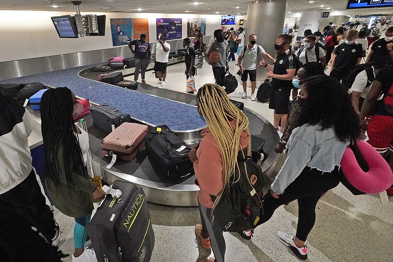 FILE - In this May 28, 2021 file photo, travelers wait for their luggage at a baggage carousel at Miami International Airport in Miami.  The airline industry’s recovery from the pandemic passed a milestone as more than 2 million people streamed through U.S. airport security checkpoints on Friday for the first time since early March 2020.  (AP Photo/Wilfredo Lee, File)