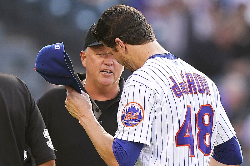 Third base umpire Ron Kulpa, left, looks inside the cap of Mets starting pitcher Jacob deGrom after the top of the fifth inning of Monday's game against the Braves in New York.