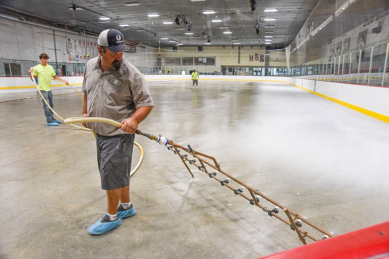 Troy Schulte pulls the paint sprayer Monday as he and fellow Jefferson City Parks co-workers replace the ice that was ruined in the recent flash flooding at Washington Park Ice Arena. 