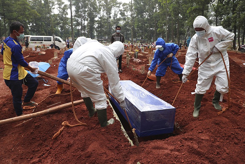 Workers in protective gear lower a coffin of a COVID-19 victim to a grave for burial at the Cipenjo Cemetery in Bogor, West Java, Indonesia, Wednesday, July 14, 2021. The world's fourth most populous country has been hit hard by an explosion of COVID-19 cases that have strained hospitals on the main island of Java. (AP Photo/Achmad Ibrahim)