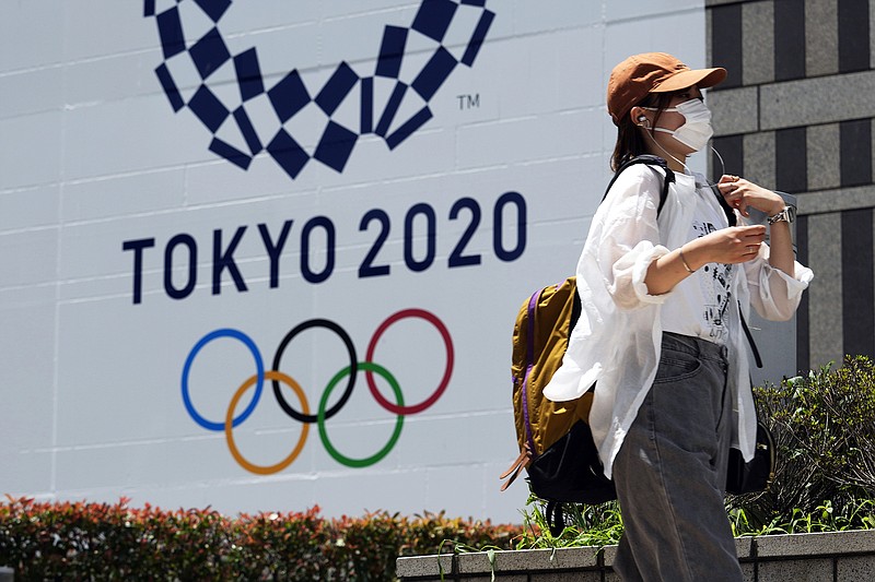 A woman wearing a protective mask walks in front of a Tokyo 2020 Summer Olympics display Tuesday at the Tokyo Metropolitan government building in Tokyo.