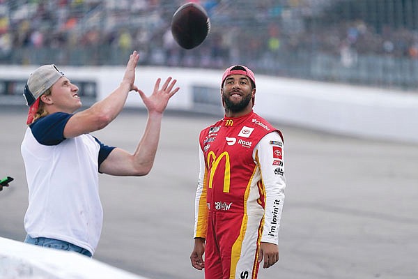 Bubba Wallace smiles while watching Patriots wide receiver Gunner Olszewski catch a football thrown by a fan during a rain delay Sunday at the NASCAR Cup Series in Loudon, N.H.