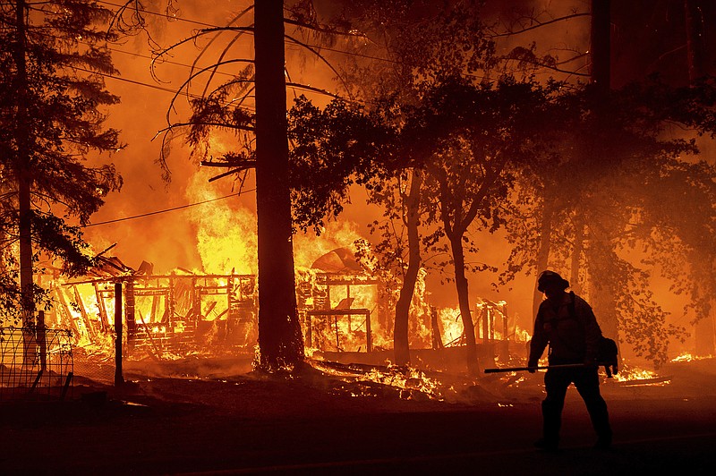 FILE - In this Saturday, July 24, 2021, file photo a firefighter passes a burning home as the Dixie Fire flares in Plumas County, Calif. The fire destroyed multiple residences as it tore through the Indian Falls community. Erratic winds and the potential for dry lightning added to the challenges facing firefighters battling California's largest wildfire, one of numerous blazes burning Monday across the U.S. West. (AP Photo/Noah Berge,File)