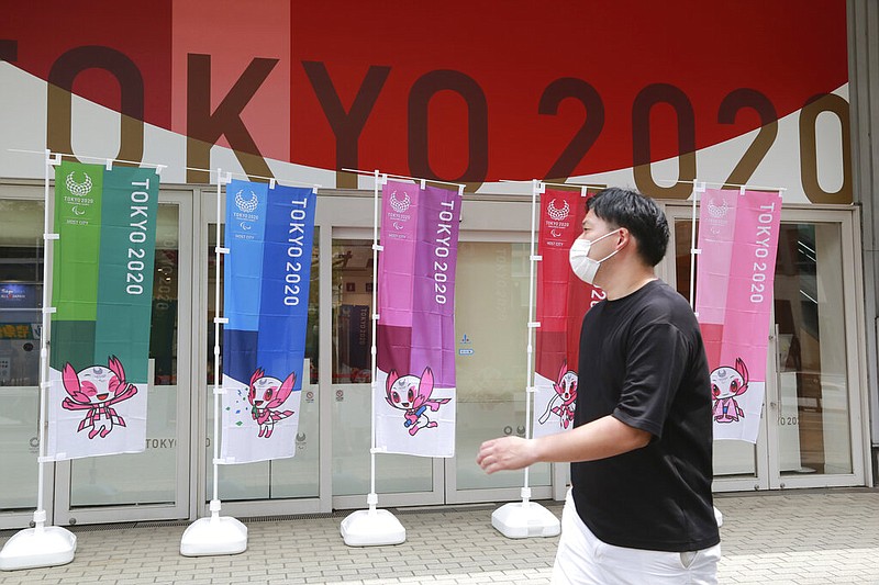 A man wearing a face mask to protect against the spread of the coronavirus walks by flags to promote the Olympic Games in Tokyo Monday, July 26, 2021. (AP Photo/Koji Sasahara)