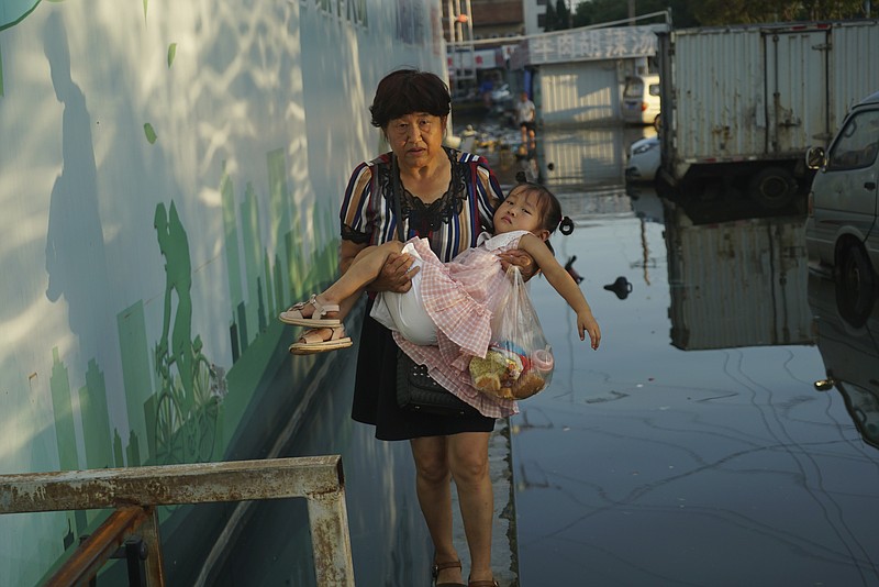 A woman carries a child in her arms as she walks on a curb above floodwaters in Xinxiang in central China's Henan Province, Monday, July 26, 2021. Record rain in Xinxiang last week left the produce and seafood market soaked in water. Dozens of people died in the floods that immersed large swaths of central China's Henan province in water. (AP Photo/Dake Kang)