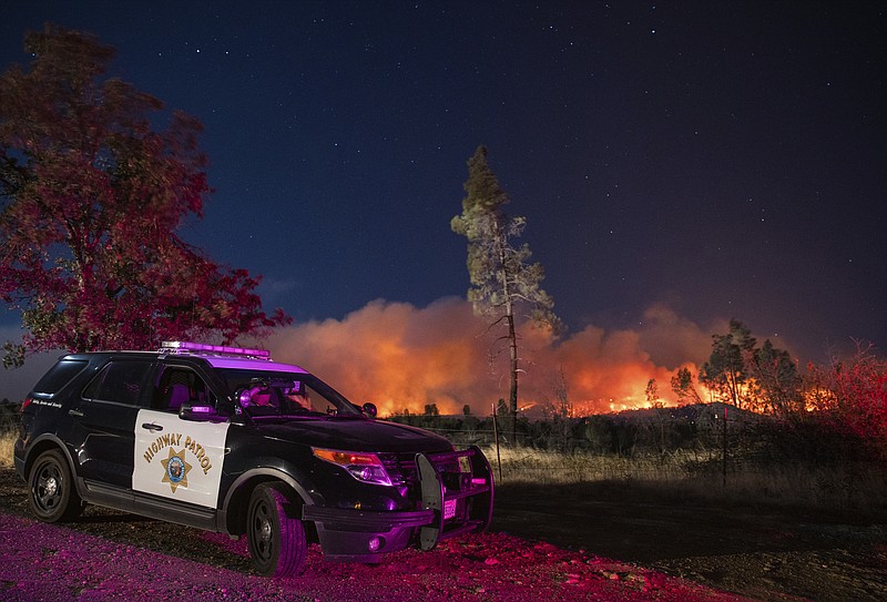 FILE - In this Sept. 28. 2020, file photo, a California Highway Patrol officer watches flames visible from the Zogg Fire near Igo, Calif. Pacific Gas & Electric will face criminal charges because its equipment sparked the wildfire that killed four people and destroyed hundreds of homes, a Northern California prosecutor announced Thursday, July 29, 2021. (AP Photo/Ethan Swope, File)