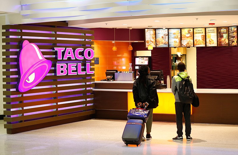 In this April 19, 2019 file photo, travelers look at a menu at a Taco Bell restaurant inside Miami International Airport in Miami. The company that owns KFC and Taco Bell posted better-than-expected sales in the second quarter thanks to stronger customer demand and a record new store building spree. (AP Photo/Wilfredo Lee, File)