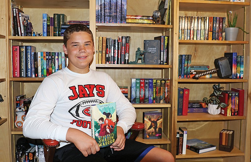 Gideon Duren, an incoming freshman at Jefferson City High School, is surrounded by numerous bookshelves in his bedroom. The shelves are usually a backdrop his video book reviews and recommendations he posts online. Duren is seen holding the book he's working his way through now,  "The Last Shadow Warrior" by Sam Subity. (Jason Strickland/News Tribune)