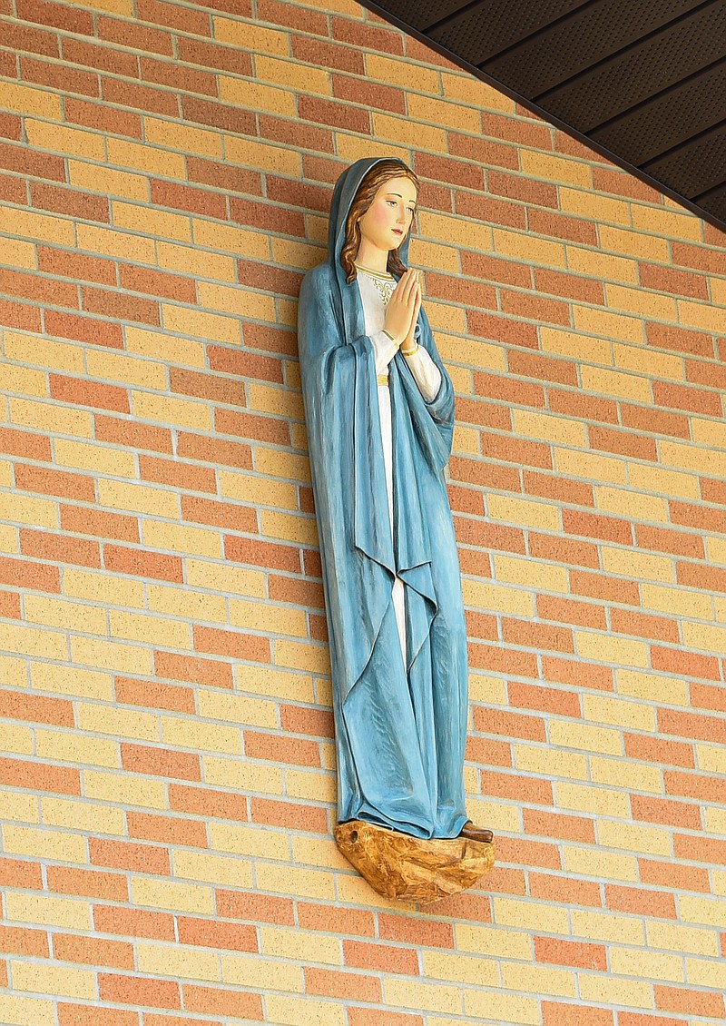 An old wooden statue of the Virgin Mary, which used to be at the old St. Mary's Hospital and most recently in storage, has been placed high on the exterior east wall of Catholic Charities of Central and Northern Missouri, where she can keep a prayerful eye over workers (seen in background installing framework for solar panels) and those who visit the facility for whatever reason.