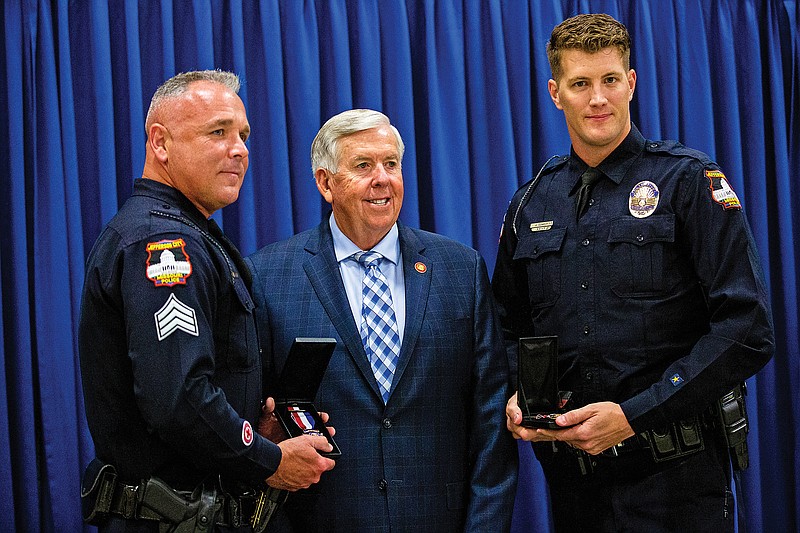 <p>Ethan Weston/News Tribune</p><p>Jefferson City Police Sgt. Michael Ottolini, left, and Officer Lee Alex Clawson, right, stand with Gov. Mike Parson on Wednesday at the Missouri State Highway Patrol Training Academy Gymnasium after receiving a Medal of Valor for acts of valor performed during the previous year. Ottolini and Clawson were awarded for “ending a threat posed by a gunman” according to the Governor’s Office.</p>