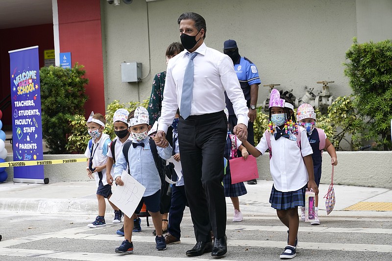 FILE- In this Aug. 23, 2021, file photo, Miami-Dade schools Superintendent Alberto Carvalho, center, walks with students Oliver Angel, left, and Ariah Olawale, right, outside of iPrep Academy on the first day of school, Monday, Aug. 23, 2021, in Miami. The on-again, off-again ban imposed by Republican Gov. Ron DeSantis to prevent mandating masks for Florida school students is back in force. The 1st District Court of Appeal ruled Friday, Sept. 10, 2021, that a Tallahassee judge should not have lifted an automatic stay two days ago that halted enforcement of the mask mandate ban. (AP Photo/Lynne Sladky, File)