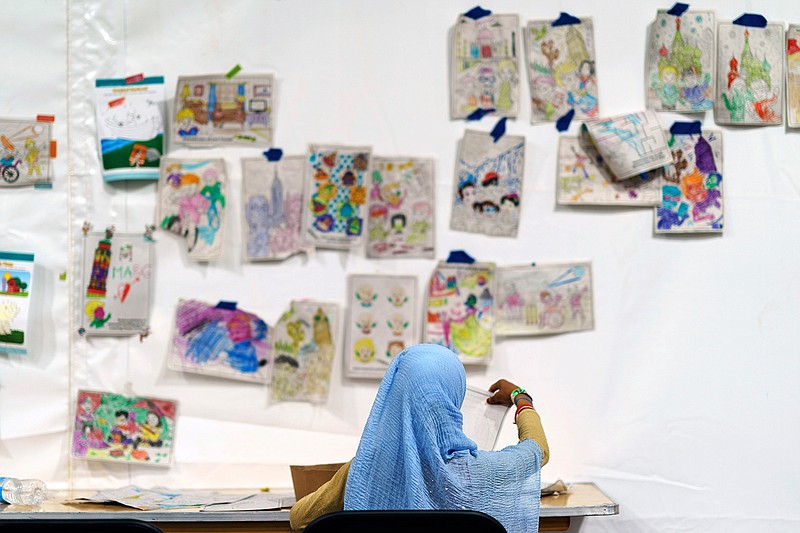 A child holds up a piece of artwork while drawing in a tent at Fort Bliss' Doa Ana Village, in New Mexico, where Afghan refugees are being housed, Friday, Sept. 10, 2021. The Biden administration provided the first public look inside the U.S. military base where Afghans airlifted out of Afghanistan are screened, amid questions about how the government is caring for the refugees and vetting them. (AP Photo/David Goldman)