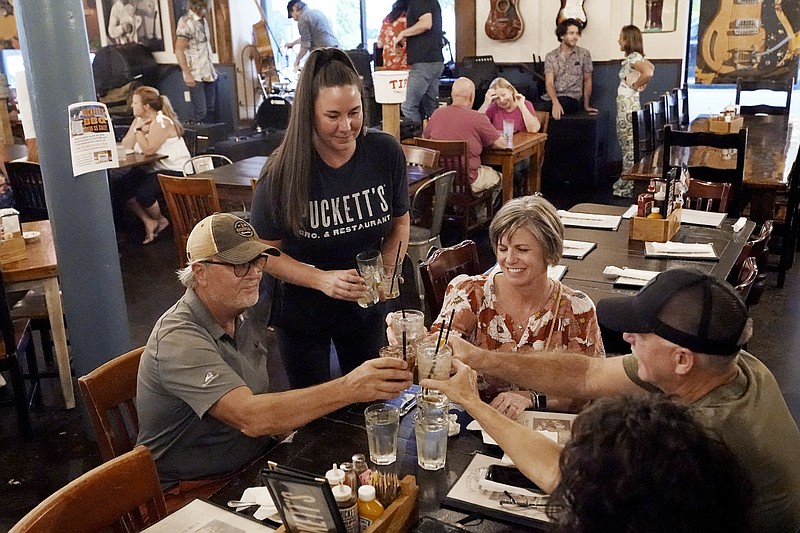 Macy Norman, center, serves a table of guests at Puckett's Grocery and Restaurant, Friday, Sept. 10, 2021, in Nashville, Tenn. In Nashville, tourism has come back faster than downtown office workers following COVID. Nashville's reputation as a tourist destination is buoying restaurants while businesses in other downtown areas have had to adapt as offices remained closed and workers stay home. (AP Photo/Mark Humphrey)